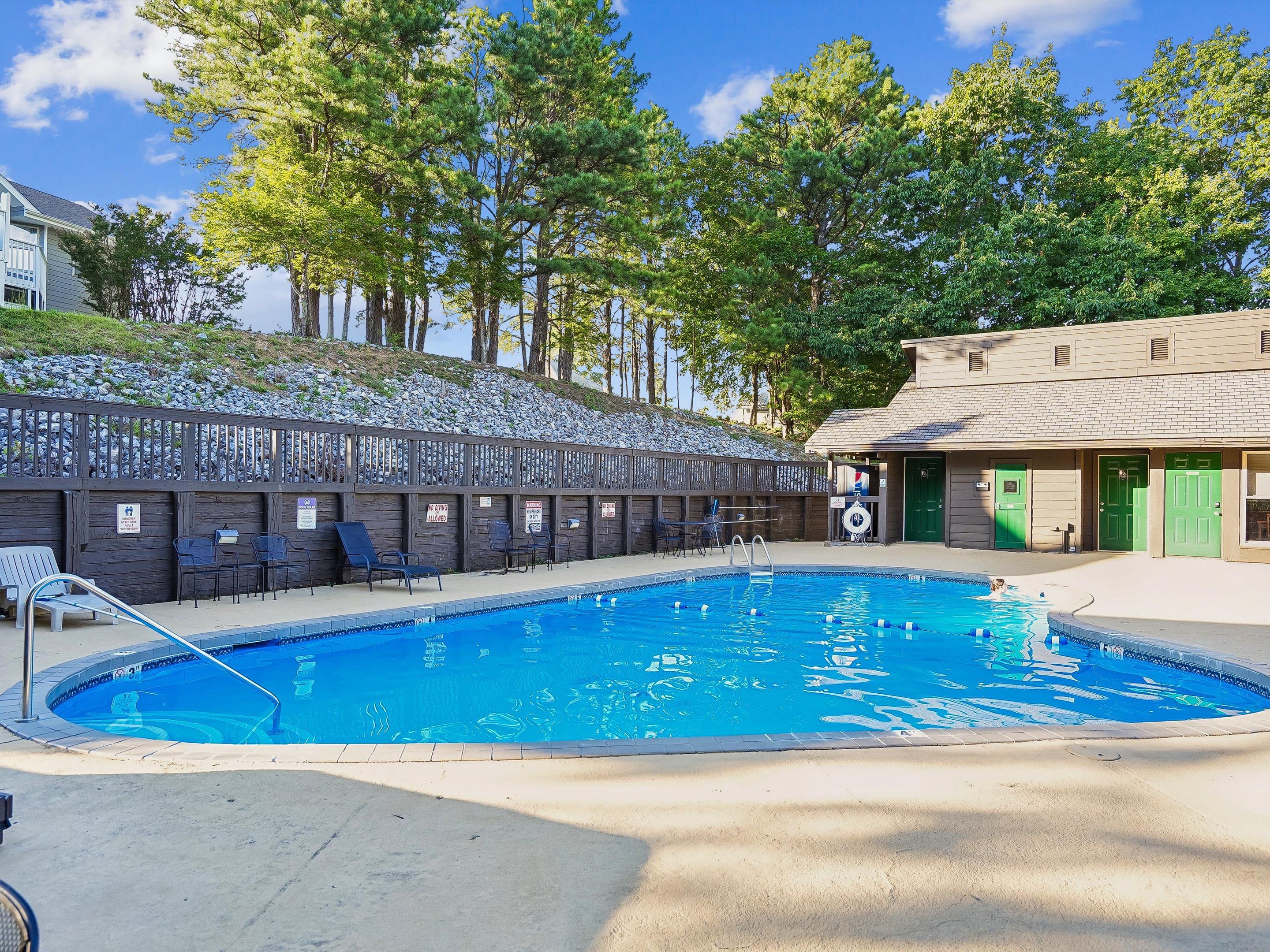A swimming pool with a wooden deck and lounge chairs, surrounded by a fence and trees.