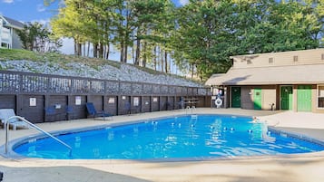Una piscina con cubierta de madera y sillas de descanso, rodeada de una valla y árboles.