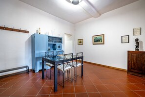 A dining area with a blue cabinet, a glass-top table, and chairs. There are wall-mounted hooks and framed pictures on the walls. - San Frediano (Florence)