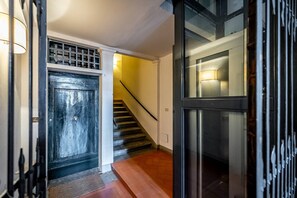 A staircase with a black door at the top, a yellow wall, and a glass door on the right. - San Frediano (Florence)