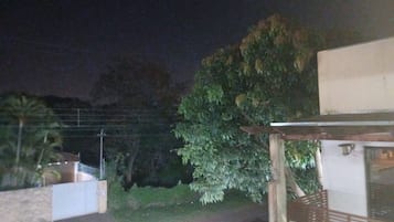 Ein Außenbereich bei Nacht mit einem gepflasterten Weg, einer hölzernen Pergola und einem weißen Gebäude.