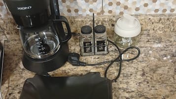 Une machine à café, des salières et des poivrières, une bouteille d’eau et une multiprise sur un plan de travail de cuisine.