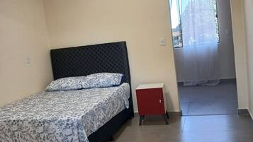 Ein Schlafzimmer mit einem Bett, einem kleinen roten Schrank und einem Fenster mit Vorhängen.