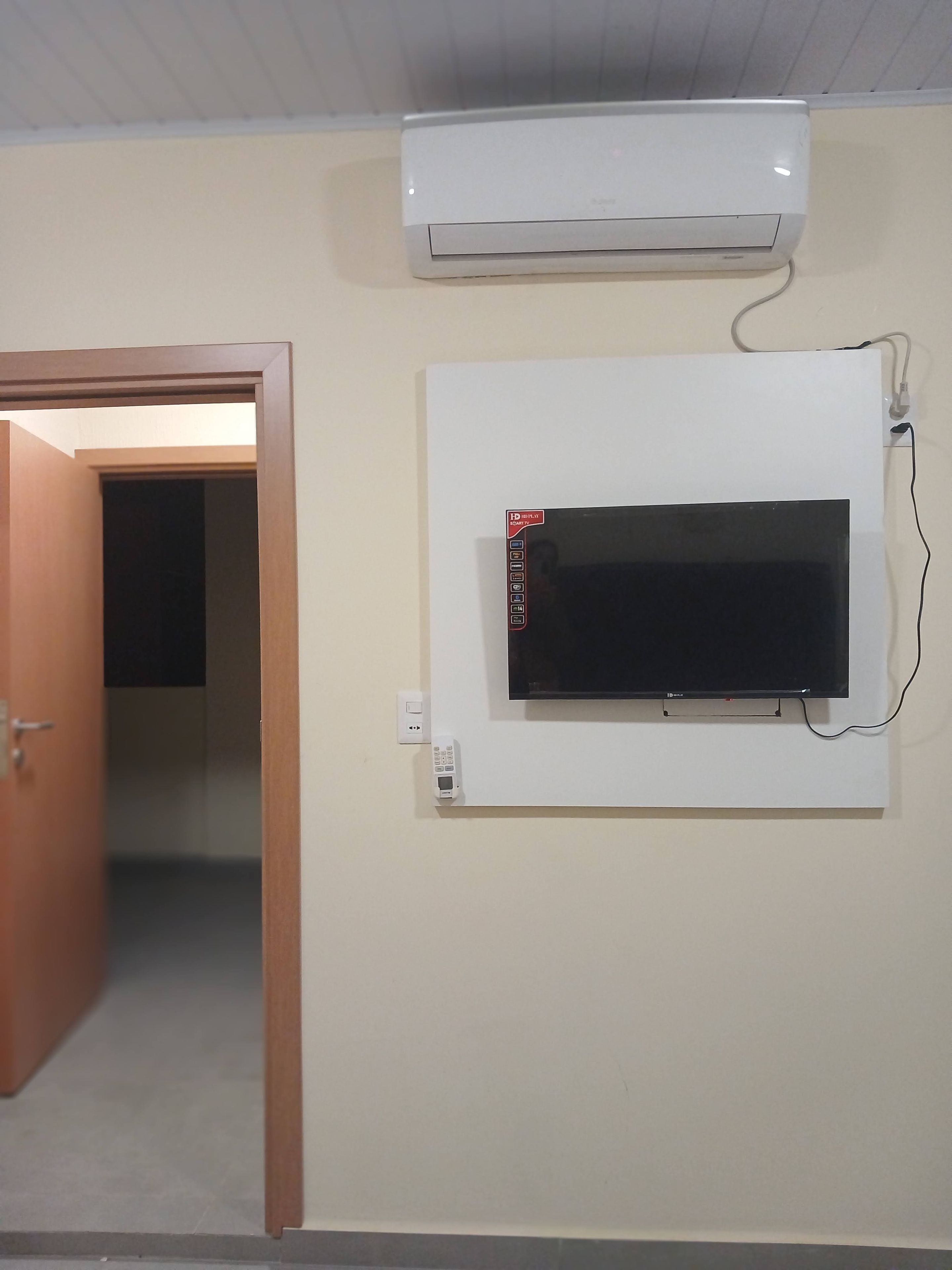 A room with a mounted flat-screen TV, an air conditioning unit, and a door leading to another room.