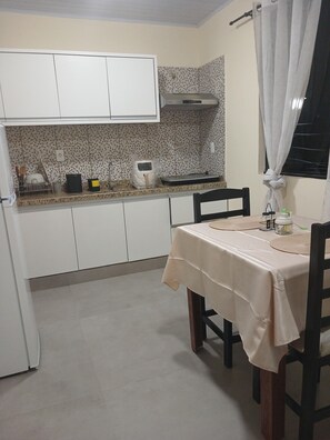 Cocina compacta con armarios blancos, una encimera con varios electrodomésticos y una mesa de comedor para dos.