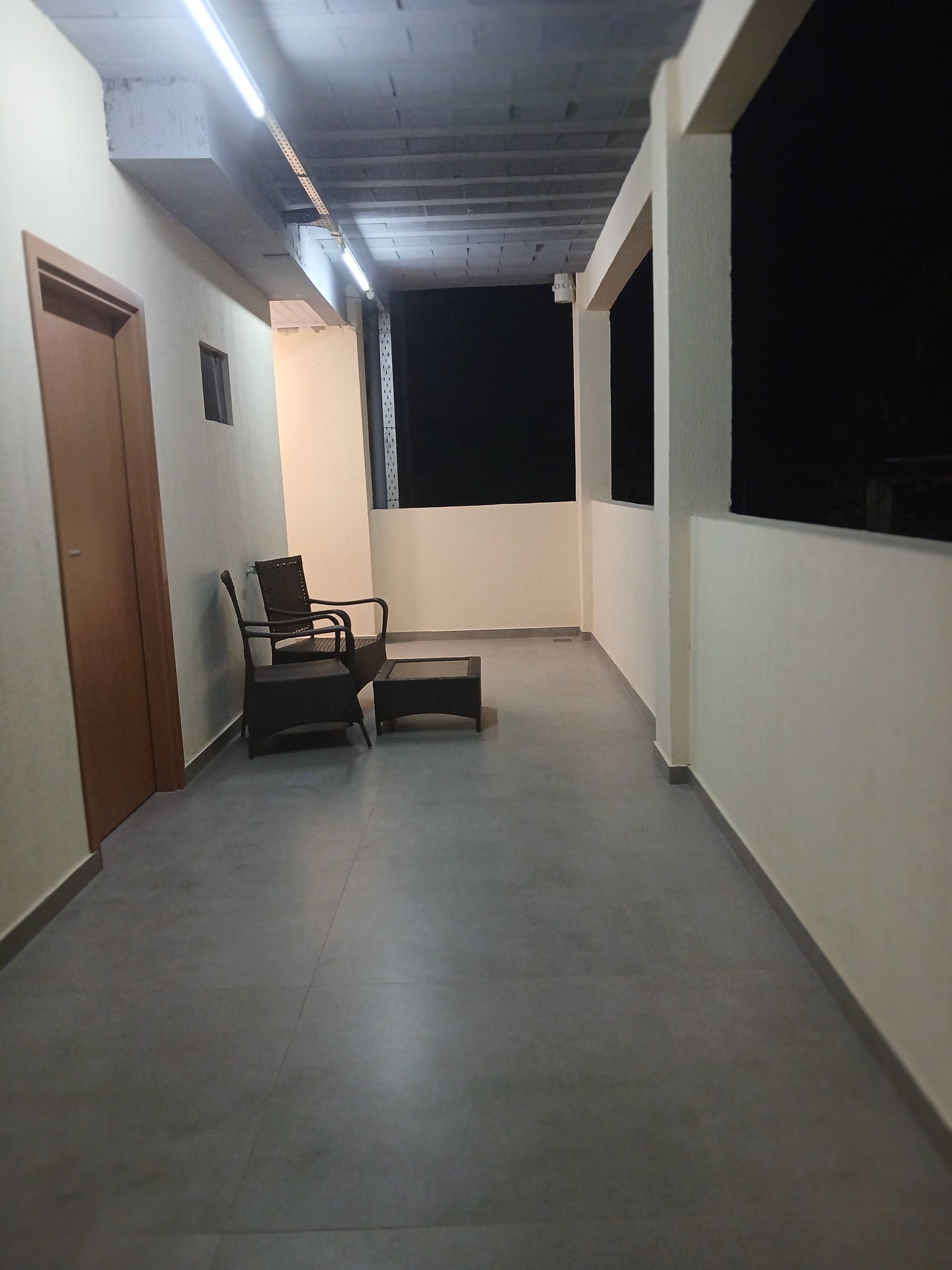 A balcony with a chair and a small table, a door, and a window.