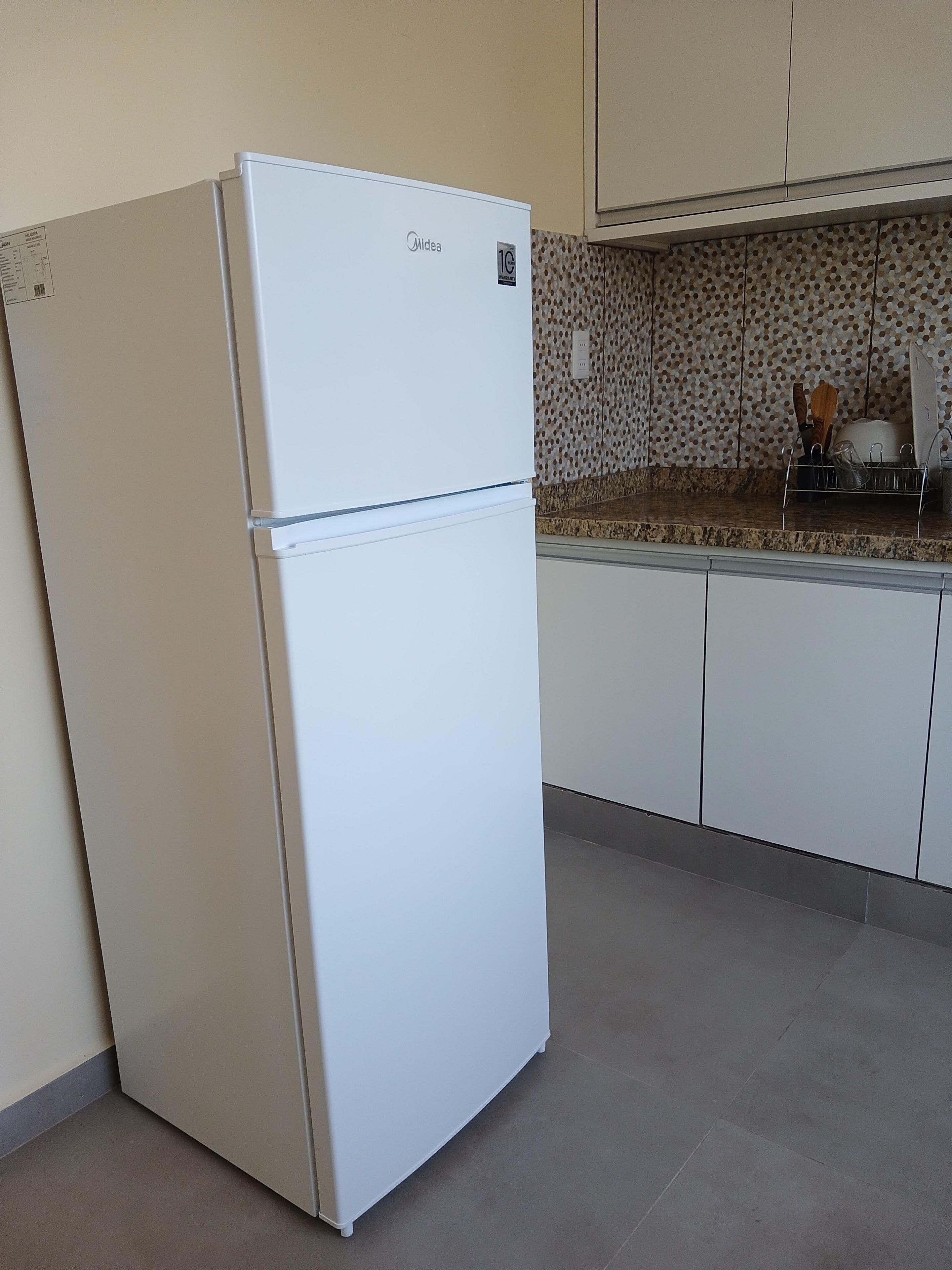 A white refrigerator in a kitchen with a tiled backsplash and a countertop with kitchen utensils.