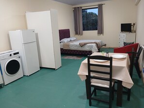 Quarto compacto com cama, mesa, cadeiras, máquina de lavar e televisão.