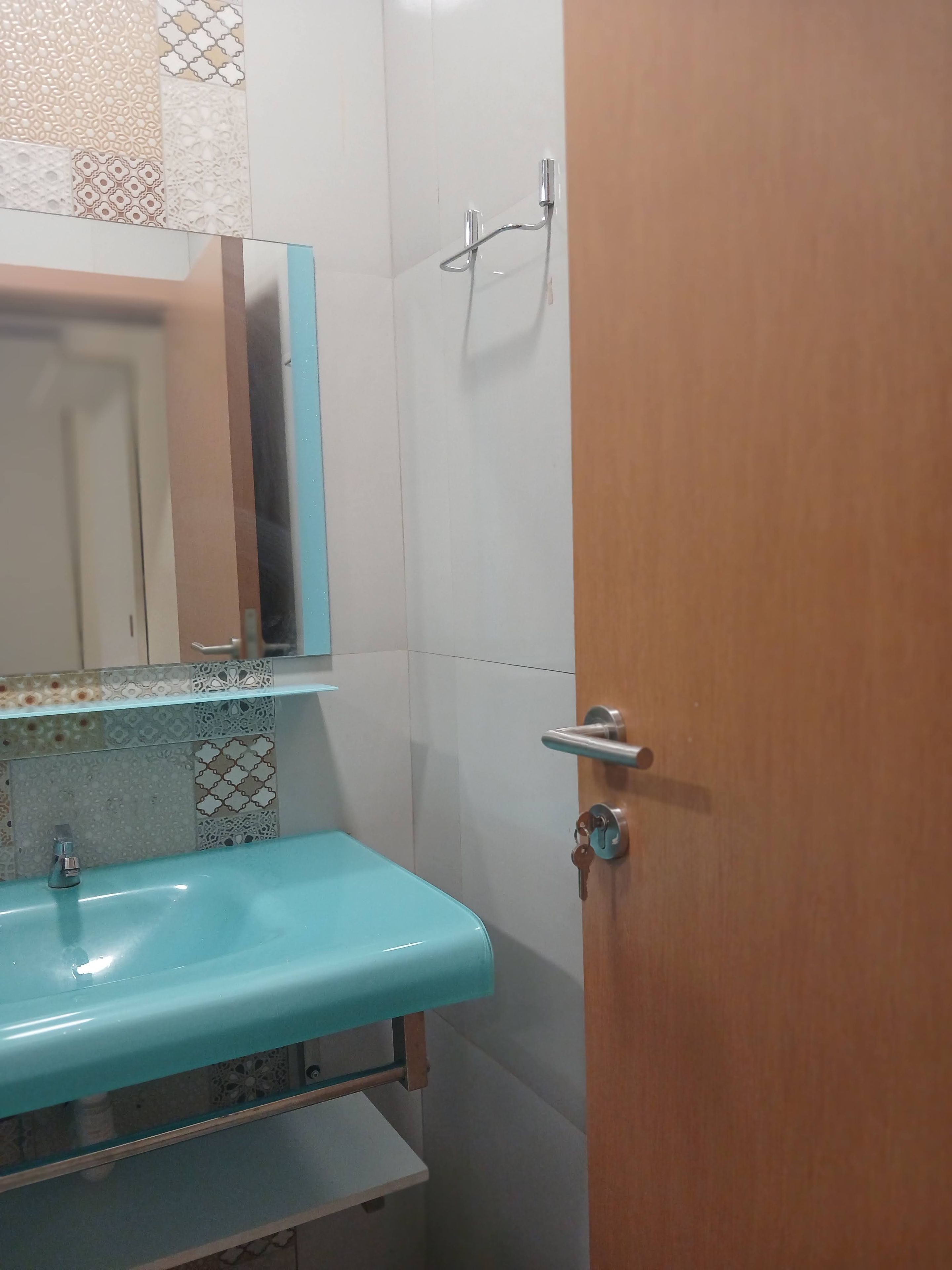 A bathroom with a sink, mirror, shower, and a door.