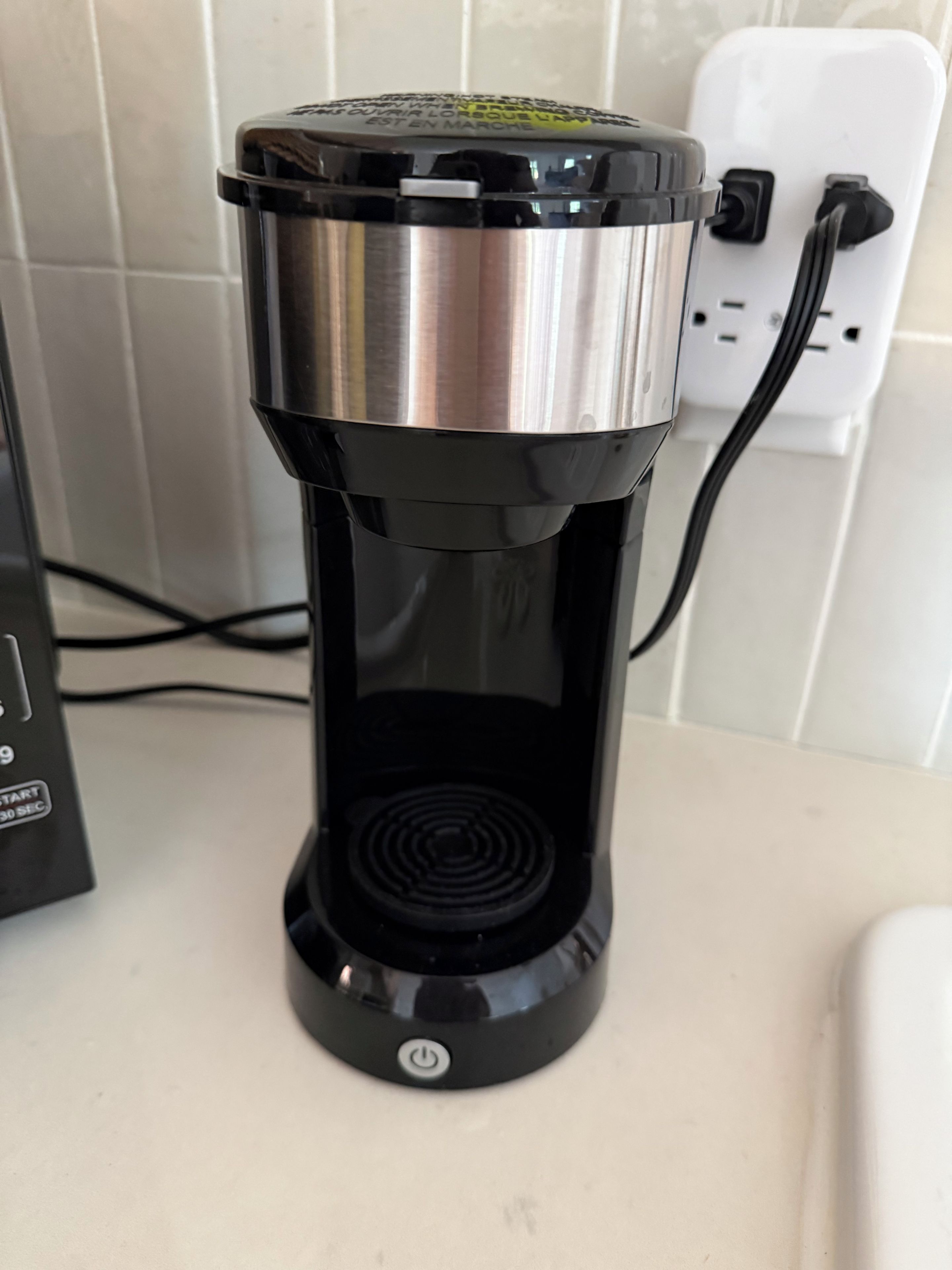 A coffee maker with a power cord plugged into a wall socket.