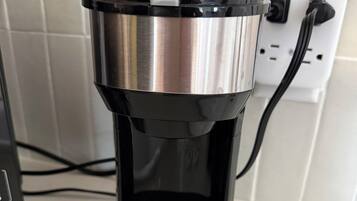 A coffee maker with a power cord plugged into a wall socket.
