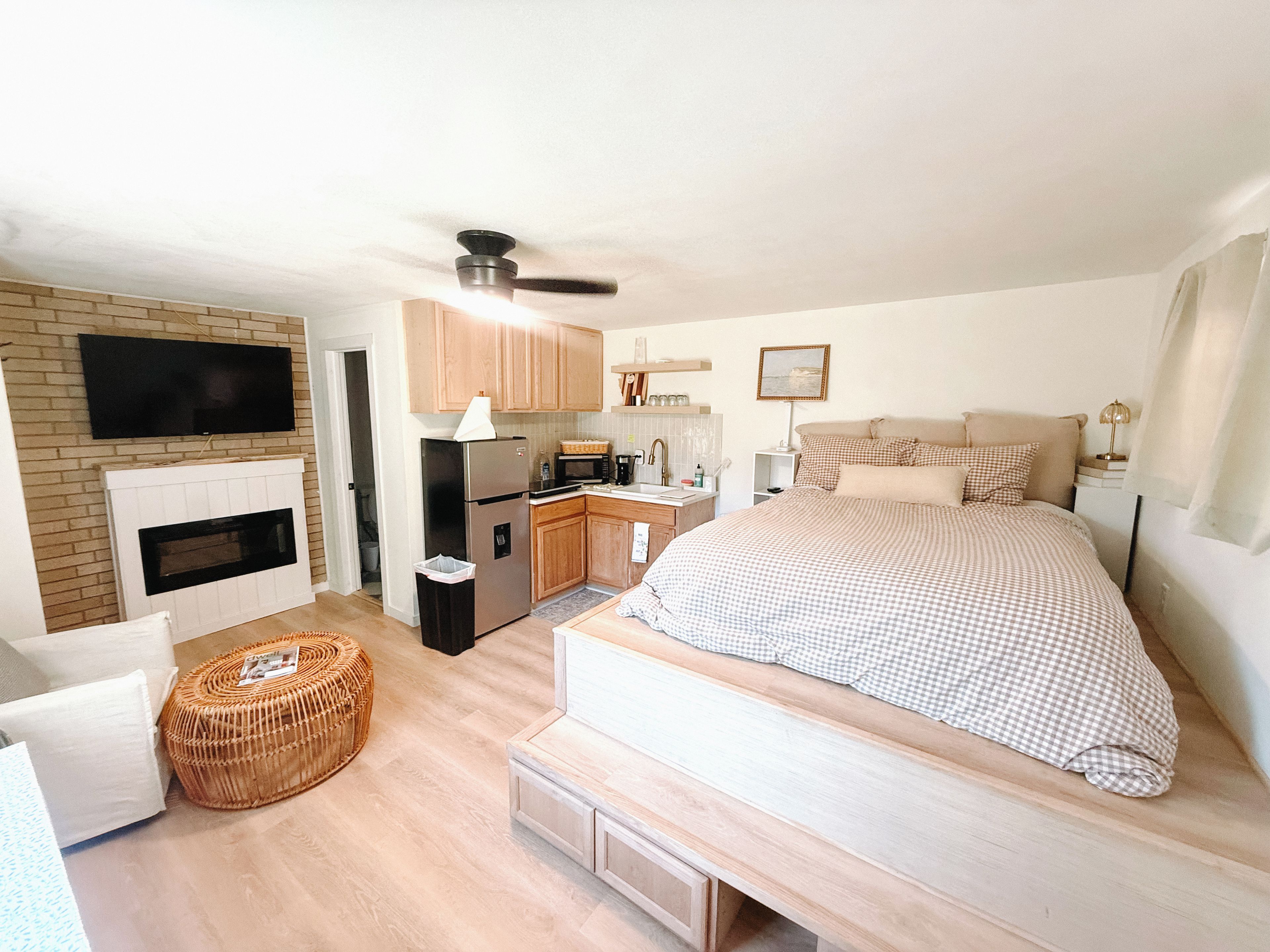 Een slaapkamer met een groot bed, een televisie boven de open haard, een keukenhoek en een plafondventilator.
