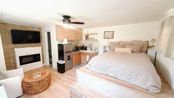Een slaapkamer met een groot bed, een televisie boven de open haard, een keukenhoek en een plafondventilator.