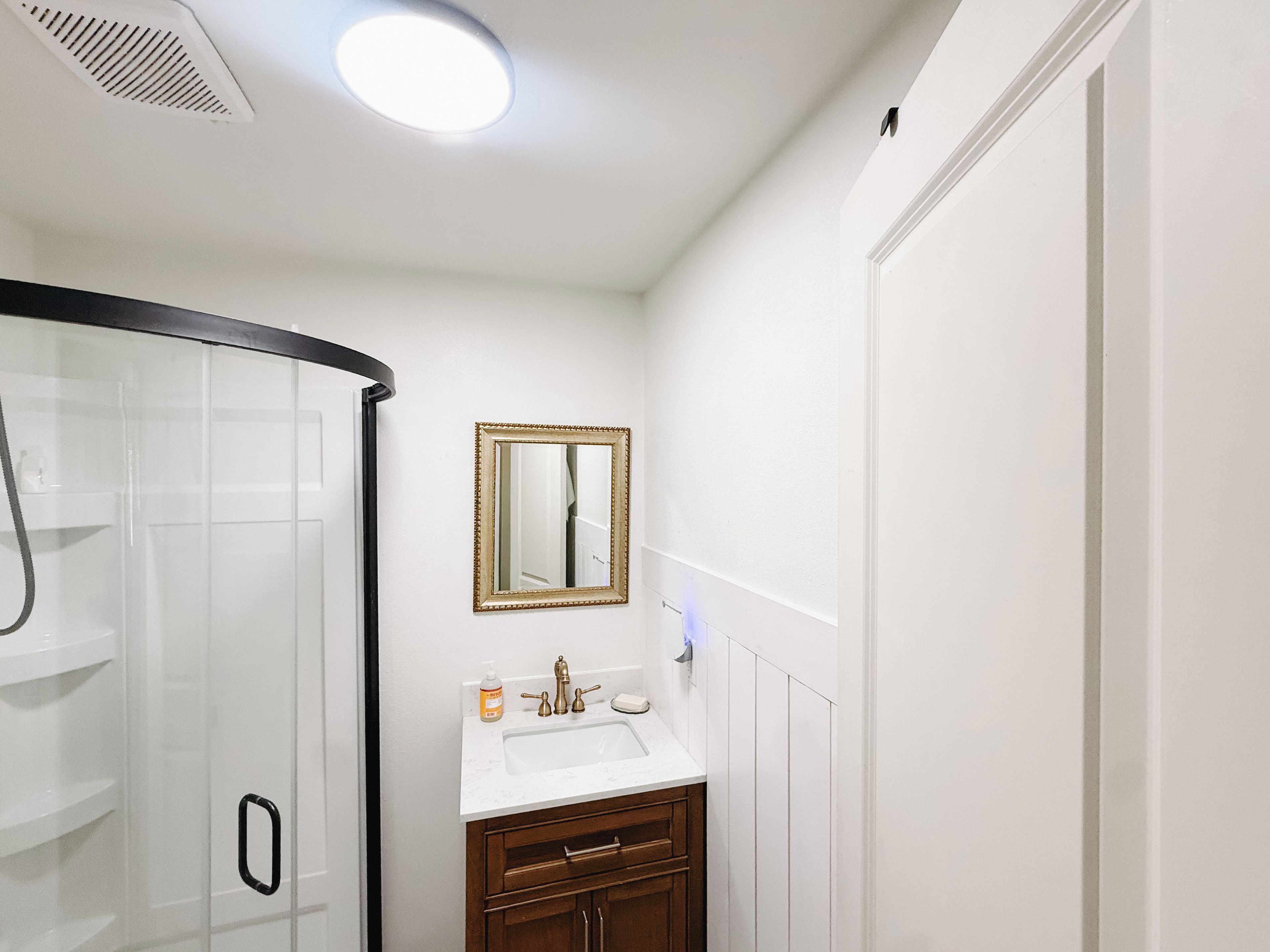 A bathroom with a glass shower enclosure, a white sink with a gold faucet, and a mirror with a gold frame.