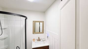 A bathroom with a glass shower enclosure, a white sink with a gold faucet, and a mirror with a gold frame.