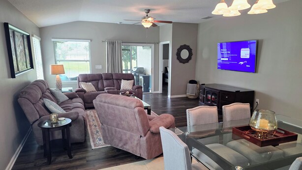 A living room with a sofa, chairs, a glass coffee table, a television, and a ceiling fan. - Modern Open Concept 3/2 Retreat (Orange Park)