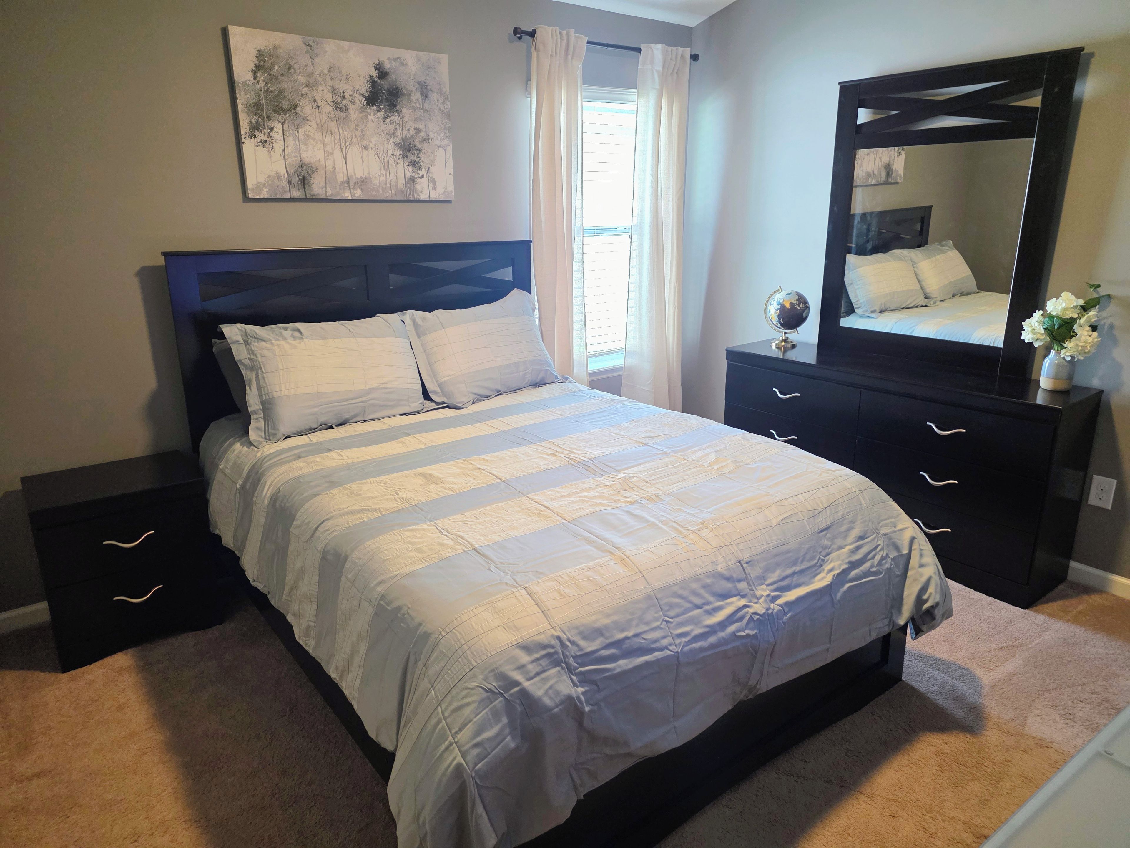 A bedroom with a bed, a nightstand, a dresser, a mirror, and a painting on the wall.