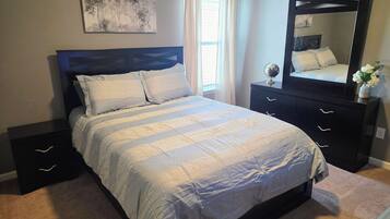 A bedroom with a bed, a nightstand, a dresser, a mirror, and a painting on the wall.