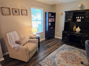 A living room with a beige sofa, a small side table with a lamp, a bookshelf, and a decorative rug.