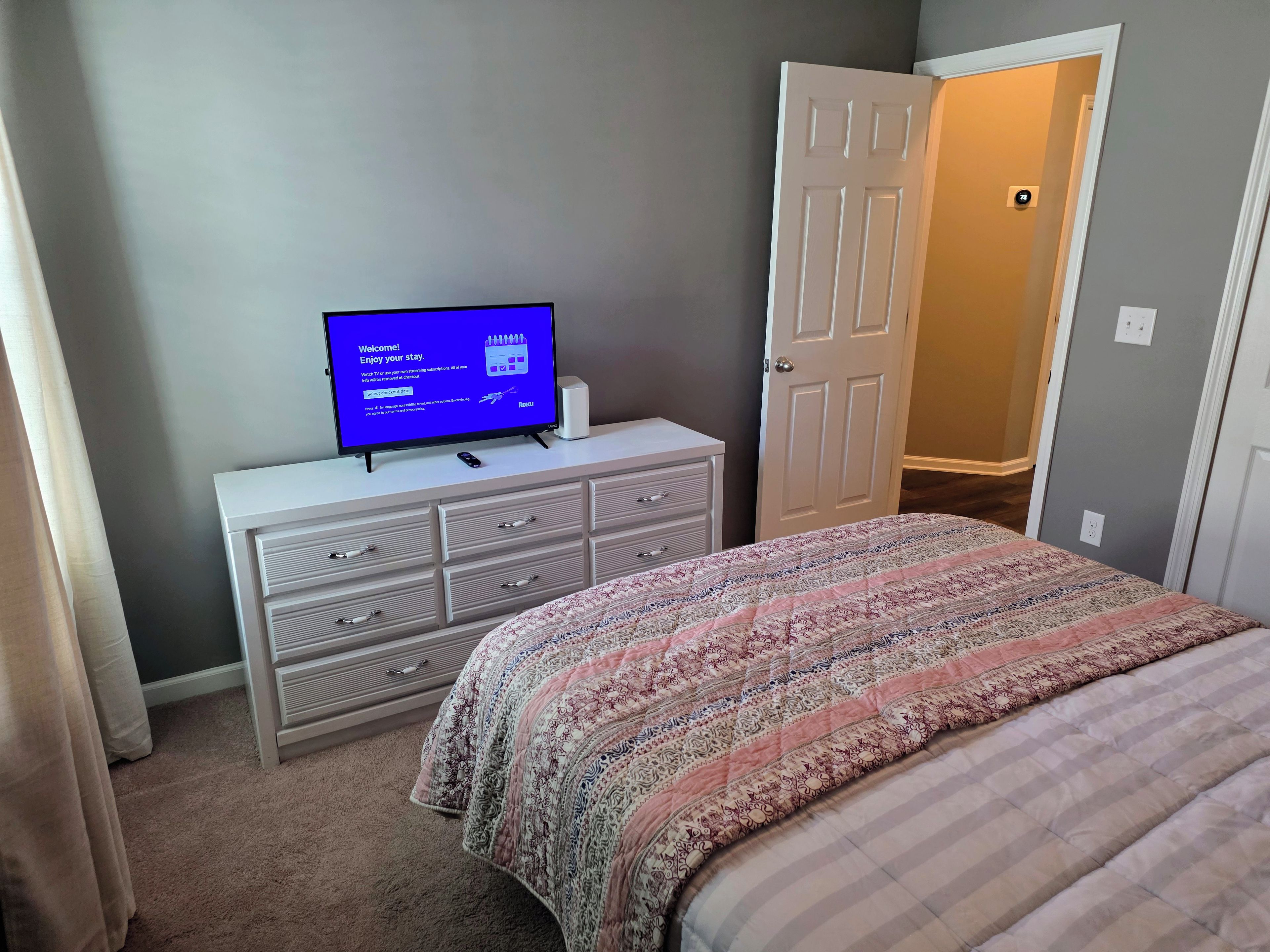 A bedroom with a bed, a dresser, a television displaying a welcome message, and a door leading to a hallway.