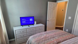 Een slaapkamer met een bed, een dressoir, een televisie waarop een welkomstbericht staat en een deur die naar een gang leidt.