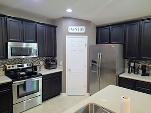 A kitchen with dark cabinets, a stainless steel refrigerator, a microwave, an oven, and a toaster.