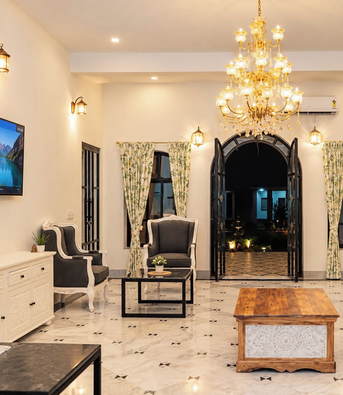Sala de estar bem iluminada com um candelabro, uma televisão e vista para uma área externa através de um arco.