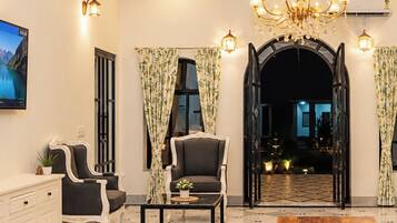 Sala de estar bem iluminada com um candelabro, uma televisão e vista para uma área externa através de um arco.