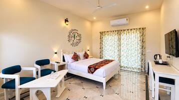 A hotel room with a bed, a desk, a chair, a nightstand, a wall-mounted TV, and an air conditioning unit.