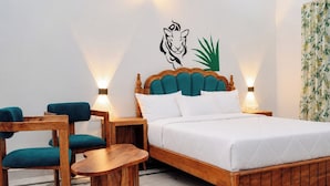 A hotel room with a bed, two chairs, a small table, and a wall with a decorative animal and plant. - Kesar Bagh  (Ranakpur)