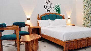 Quarto de hotel com cama, duas cadeiras, uma mesinha e parede decorada com animais e plantas.