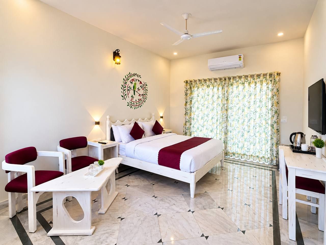 Quarto de hotel com cama, escrivaninha, cadeira, mesa pequena, televisão e ar condicionado.