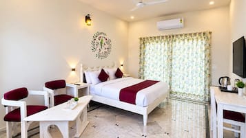 Quarto de hotel com cama, escrivaninha, cadeira, mesa pequena, televisão e ar condicionado.