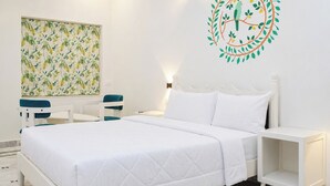 A hotel room with a bed, a nightstand, a chair, a wall art piece, and a decorative wall decal. - Kesar Bagh  (Ranakpur)