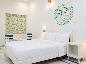 Una habitación de hotel con cama, mesita de noche, silla, una obra de arte en la pared y un adhesivo decorativo.