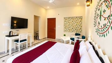 Quarto de hotel com cama, escrivaninha, cadeira, televisão e um adorno na parede.