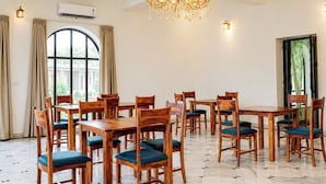A spacious dining area with wooden tables and chairs, a chandelier, and a ceiling fan. - Kesar Bagh  (Ranakpur)