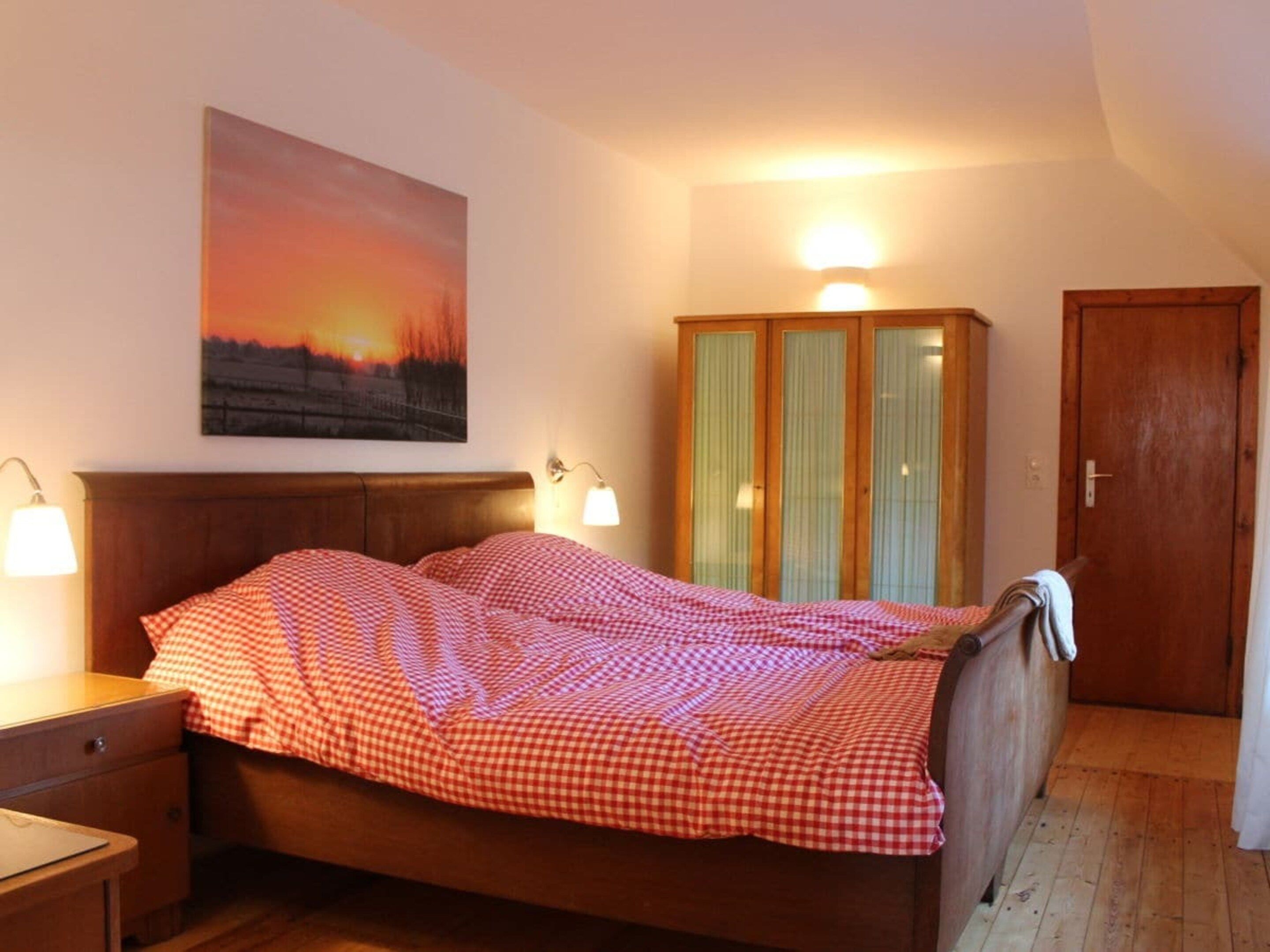 A bedroom with a bed, bedside lamps, a wooden wardrobe, and a painting on the wall.