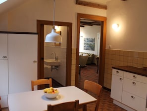 A dining area with a table, chairs, a bowl of fruit, a white pendant light, and a view into a living room through an open doorway. - Holiday Home With 5 Bedrooms (Osterholz-Scharmbeck)