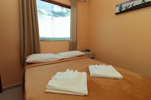 A hotel room with a bed, a window with curtains, a nightstand, and a painting on the wall.