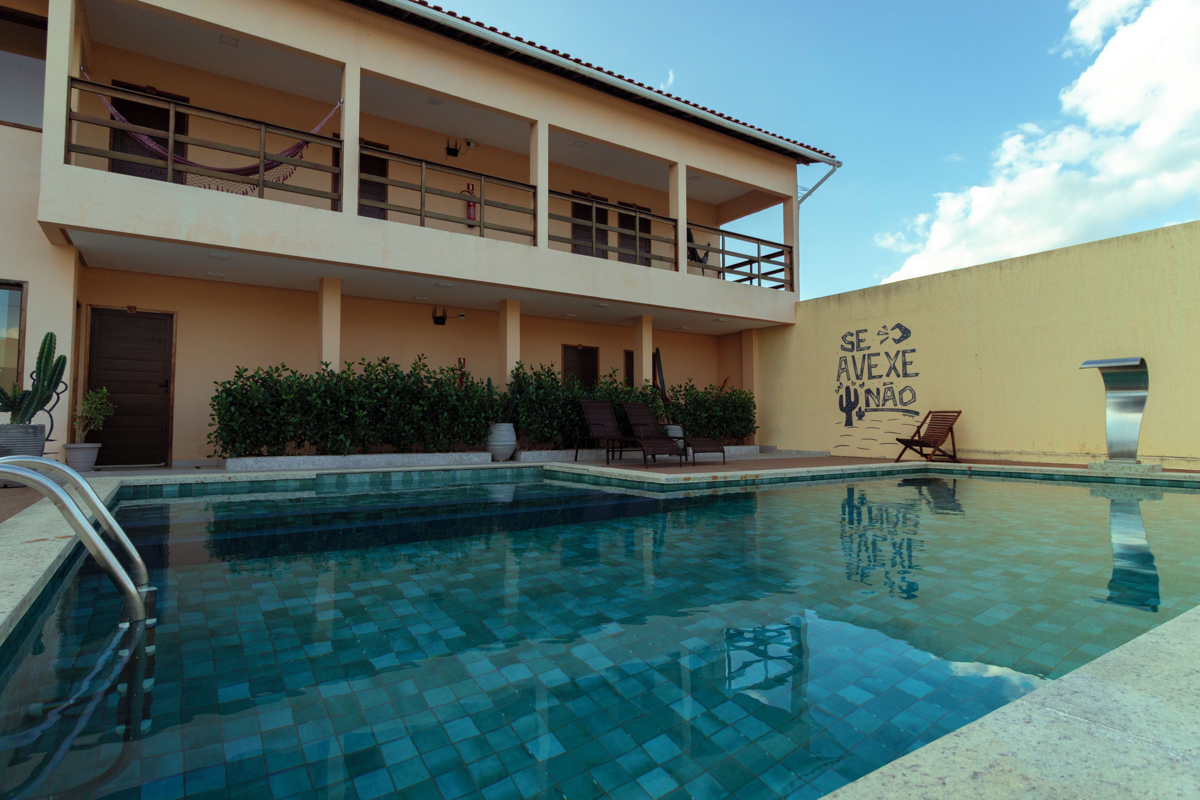 Um hotel com piscina, varanda com cadeiras de descanso e parede com um mural.