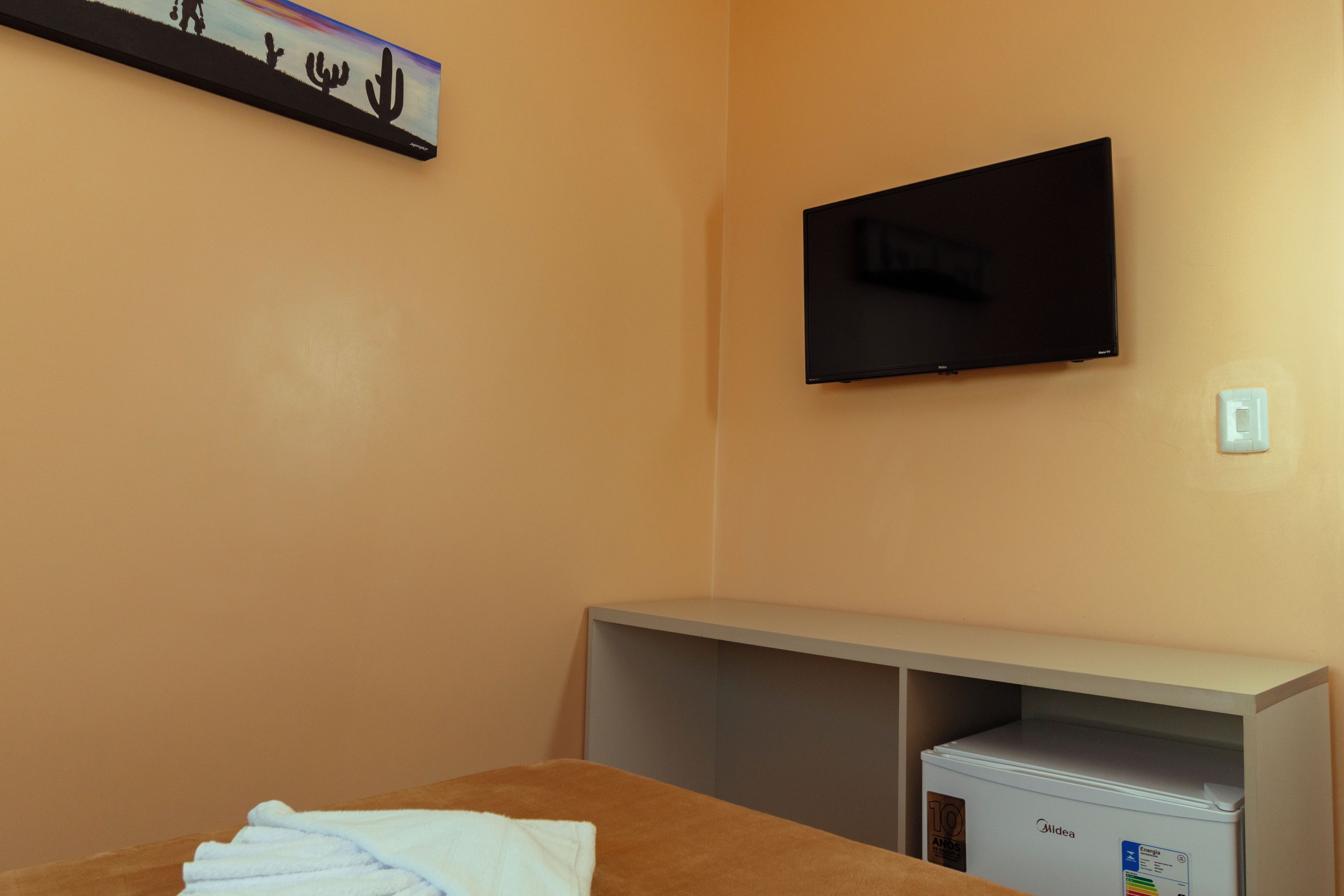 A hotel room with a bed, a television mounted on the wall, and a minibar.