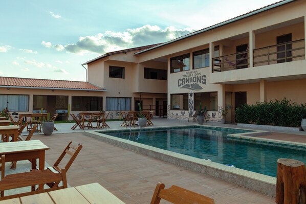 A hotel with a swimming pool, outdoor seating, and a sign reading 'Pousada Trilha dos Canions'.