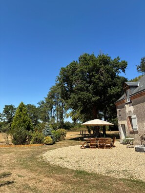 Um pátio com mesa e cadeiras, rodeado por árvores e um edifício.
