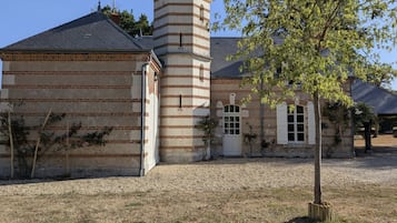 A building with a brick facade, a tower with a conical roof, and a tree in the foreground.