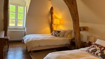 A room with two beds, a window, wooden beams, and a radiator.