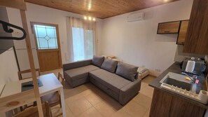 Un espacio habitable compacto con sofá, una mesa de comedor, una zona de cocina con lavaplatos y una ventana con cortinas.