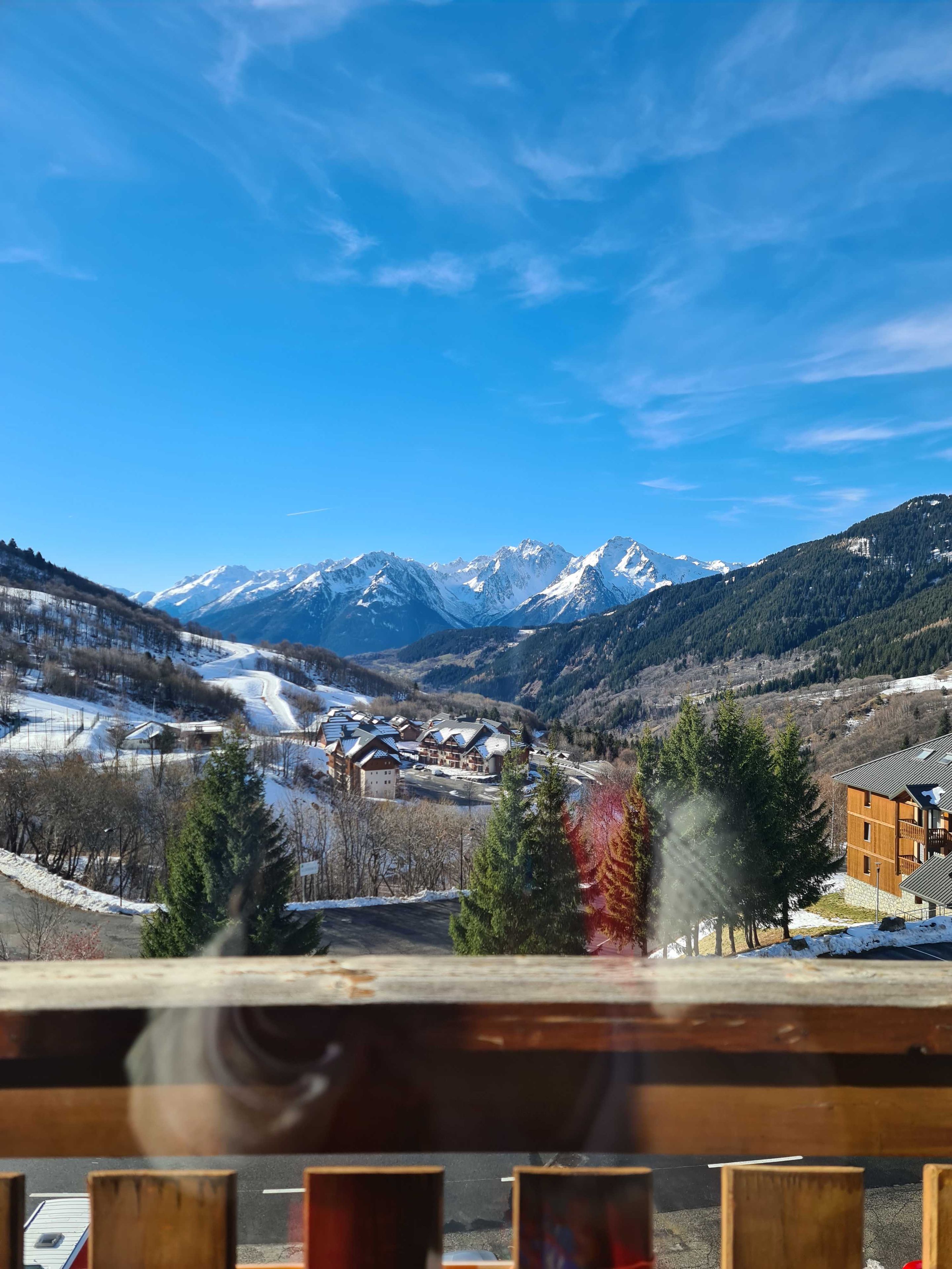 A mountain resort with snow-covered peaks, a ski slope, and a building with a wooden facade.