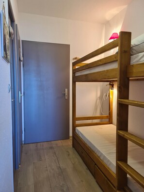 A bunk bed with a wooden frame and a mattress, a door with a handle, and a wooden floor. - Ski Access Apartment w/ Mountain Views & Balcony (Saint François Longchamp)