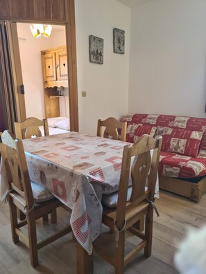 A dining area with a table set for four, wooden chairs, and a red and white patterned sofa in the background. - Ski Access Apartment w/ Mountain Views & Balcony (Saint François Longchamp)